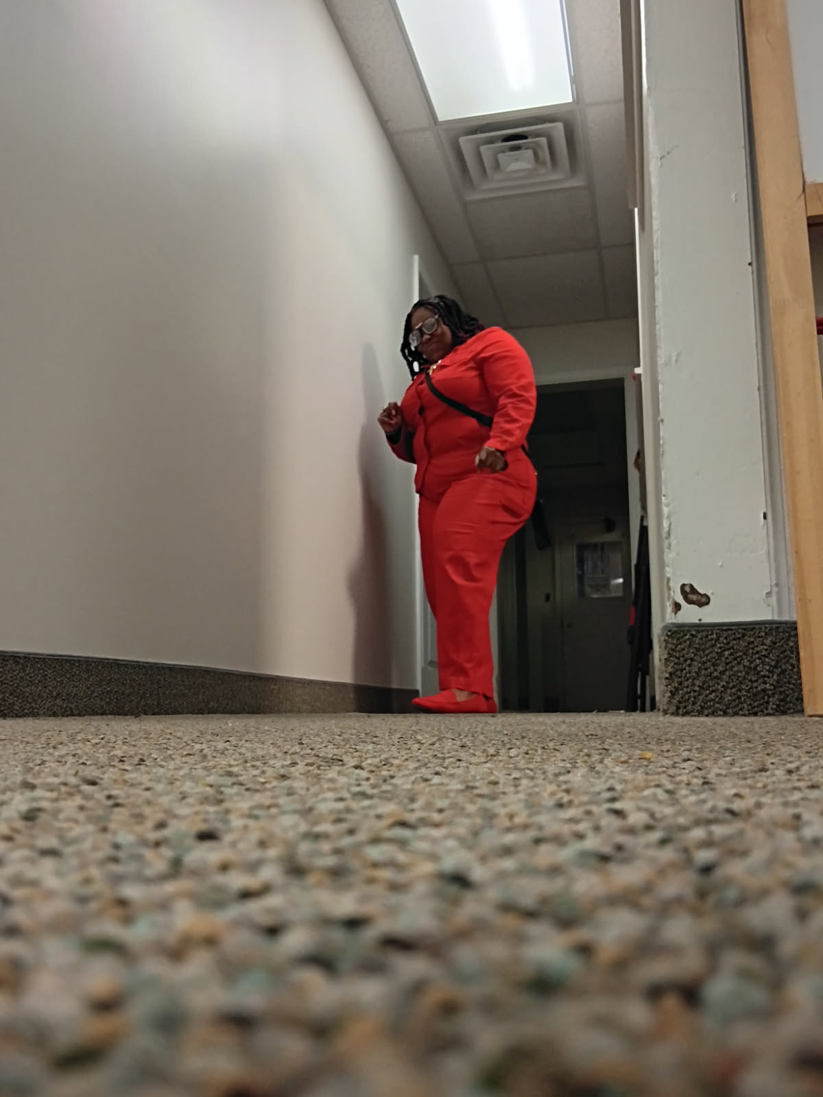 Jessica Stephens in a red suit and glasses, standing in a hallway